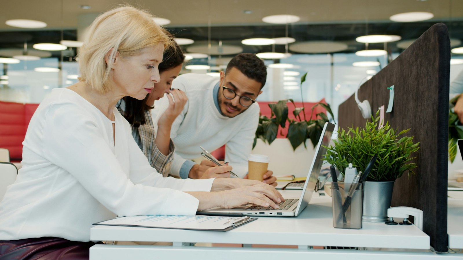 Three colleagues working together around a laptop in a shared workspace