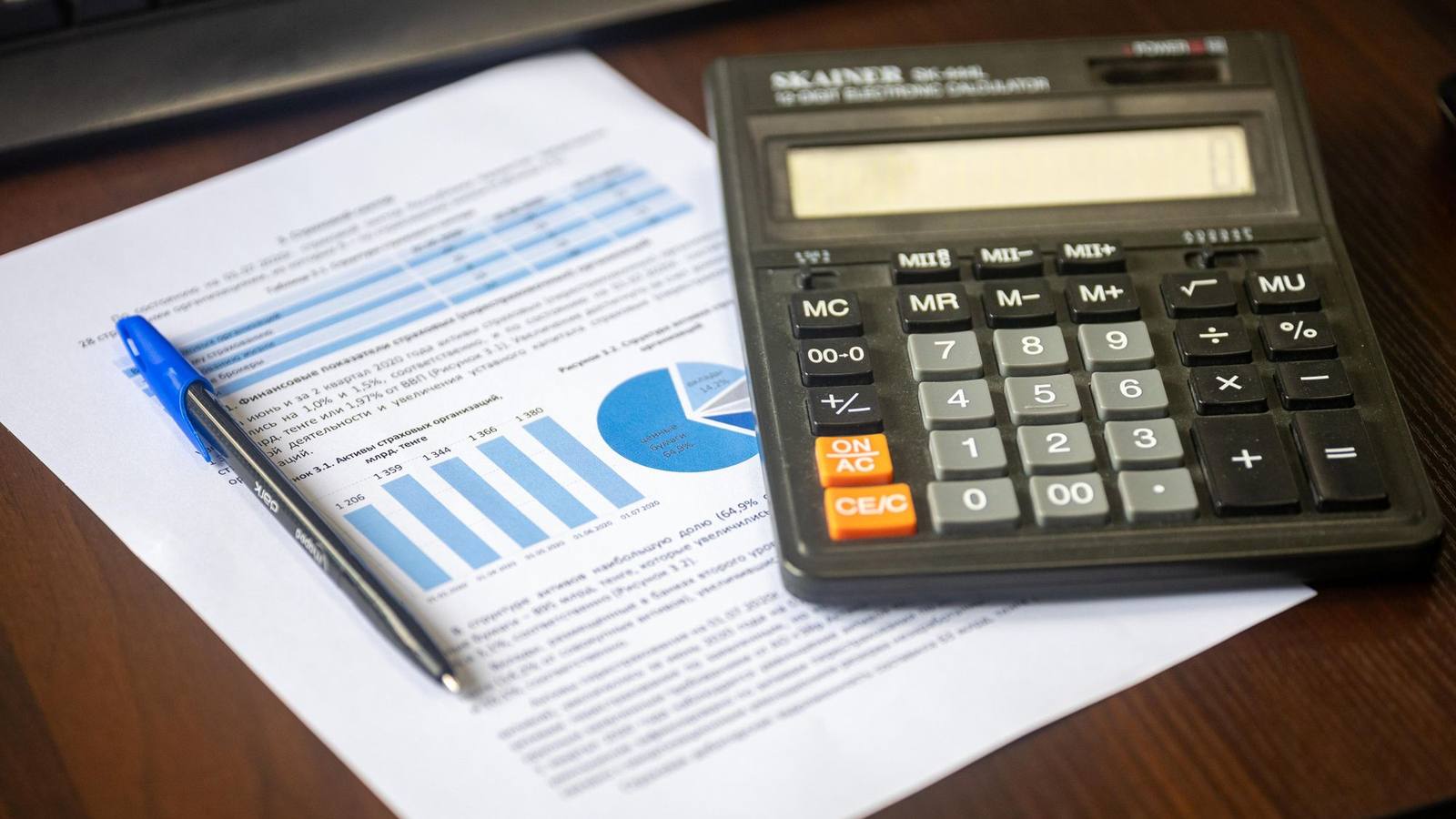 A calculator, a pen and a printed financial report on a wooden desk.