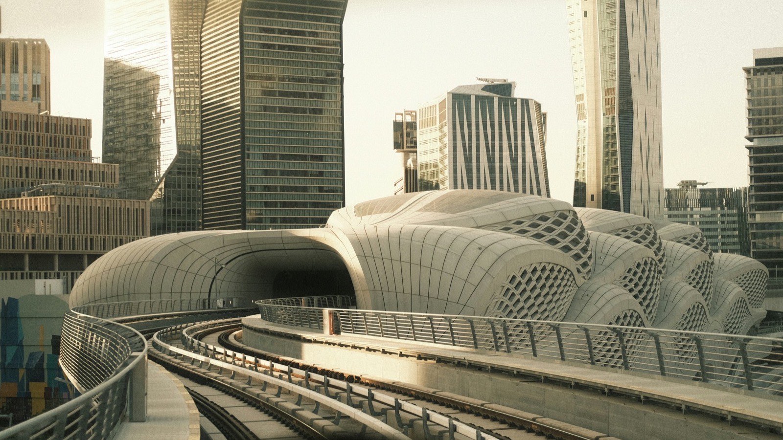 An elevated metro line curving towards a white, wave-shaped station among glass towers in Riyadh.