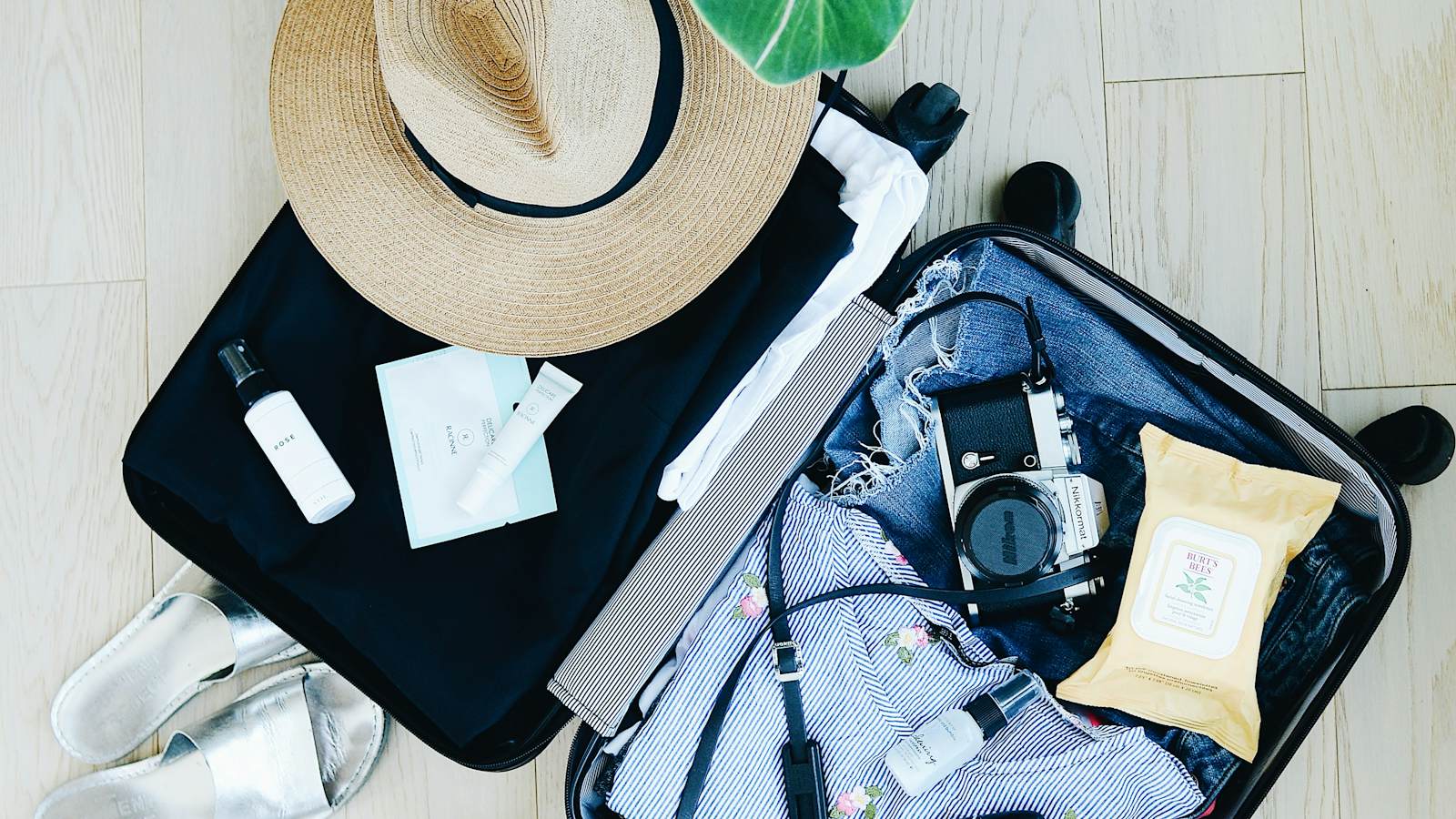 An open suitcase packed with travel essentials and a sun hat