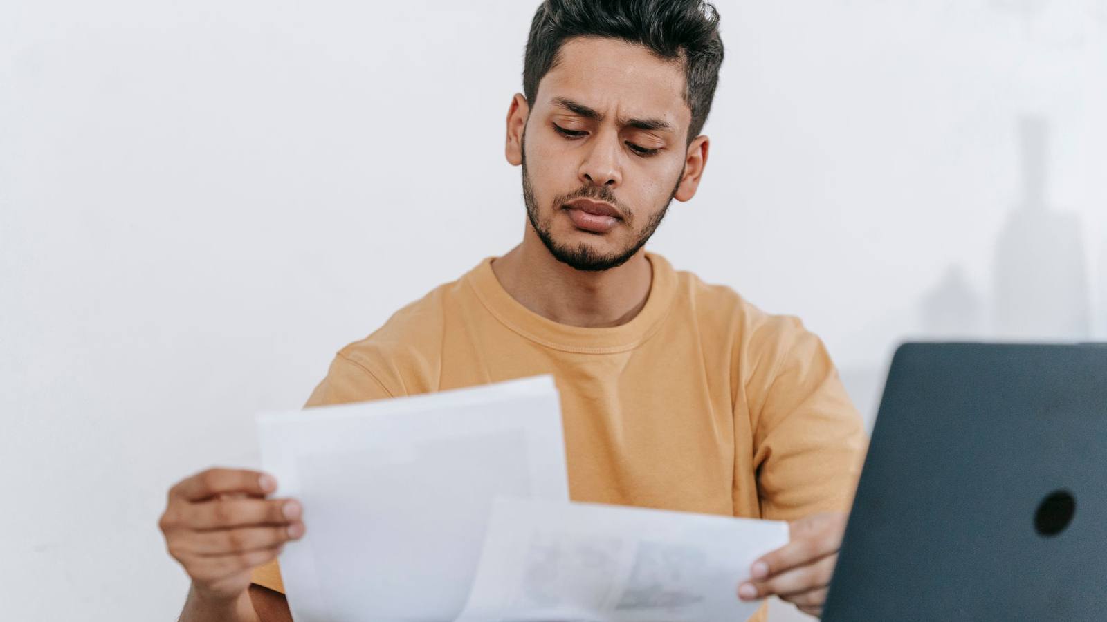 A man reviewing printed documents beside a laptop at home